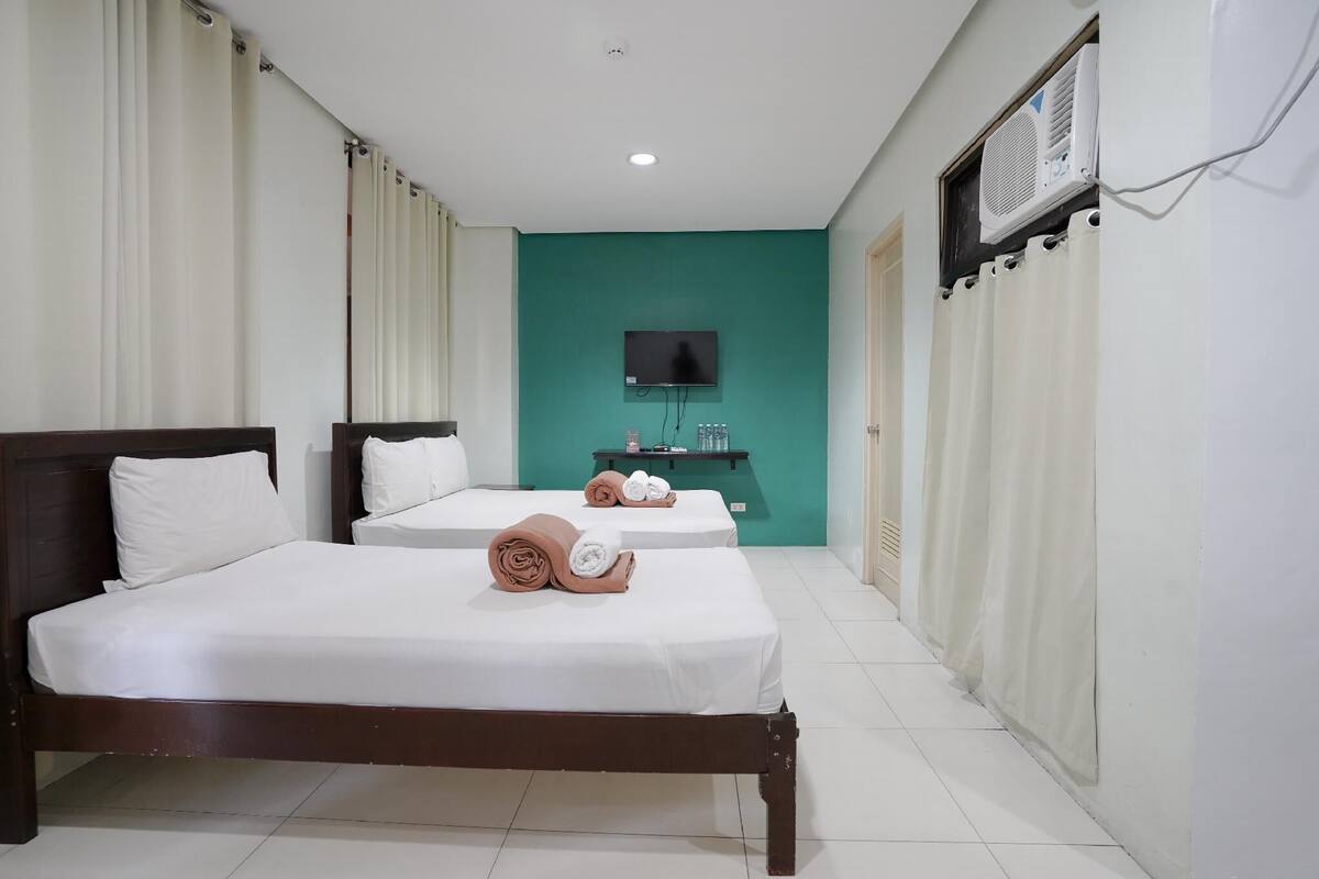 A hotel room with two beds, a television, an air conditioning unit, and a small table with toiletries.