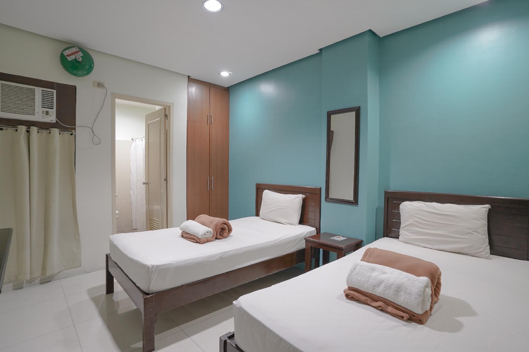 Habitación de hotel con dos camas, un armario de madera, una mesita de noche pequeña y un aire acondicionado instalado en la pared.