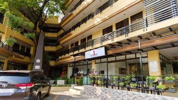 A multi-story hotel with a yellow facade, outdoor seating area, and a Toyota SUV parked in front. - Arzo Hotel Grand Lodge (Manila)