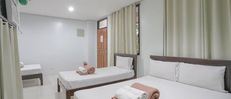 A hotel room with two single beds, a wooden headboard, a small table, and a window with curtains.