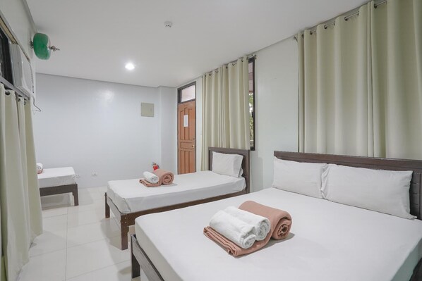 Habitación de hotel con dos camas individuales, cabecero de madera, una mesita pequeña y una ventana con cortinas.