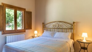 Un dormitorio con una cama, dos lámparas de noche, un ventanal con contraventanas de madera y un radiador.