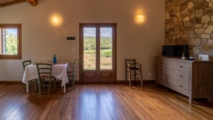 Una habitación con suelo de madera, una mesa con manteles blancos, sillas y una pared de piedra con un televisor encima.