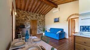 Un comedor con pared de piedra, sofá azul y cocina con salpicadero de azulejos.