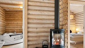 A log cabin interior with a wood-burning stove, a white toilet, and a bed in the adjacent room.