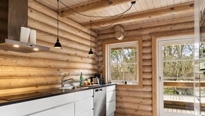 A modern kitchen with wooden walls, a black countertop, white cabinets, and a window overlooking a deck.