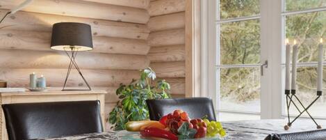 L’intérieur d’un chalet en bois, avec une table à manger, des chaises, une lampe et une vue sur l’extérieur.