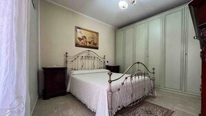 A bedroom with a bed, a nightstand, a dresser, a painting on the wall, and a chandelier. - CASA VACANZE PERLA - 6 POSTI LETTO (PARTINICO)