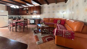 A cozy living room with a leather sofa, a dining table with chairs, and a kitchen area with wooden cabinets and a tiled backsplash. - CASA VACANZE PERLA - 6 POSTI LETTO (PARTINICO)