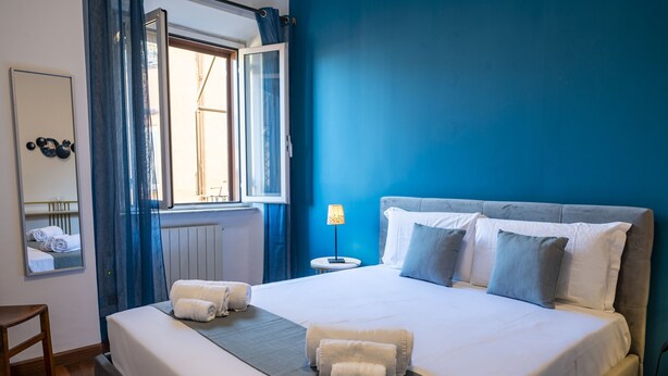 A hotel room with a large bed, a bedside table, a lamp, and a window with curtains. - Domus Otto - Large apartment close to Vatican Museums (Roma)