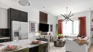 A modern kitchen with dark cabinets, a stainless steel refrigerator, and a dining area with a marble countertop. - The Hubb House – Relaxing Rooftop + Hot Tub (Nashville)