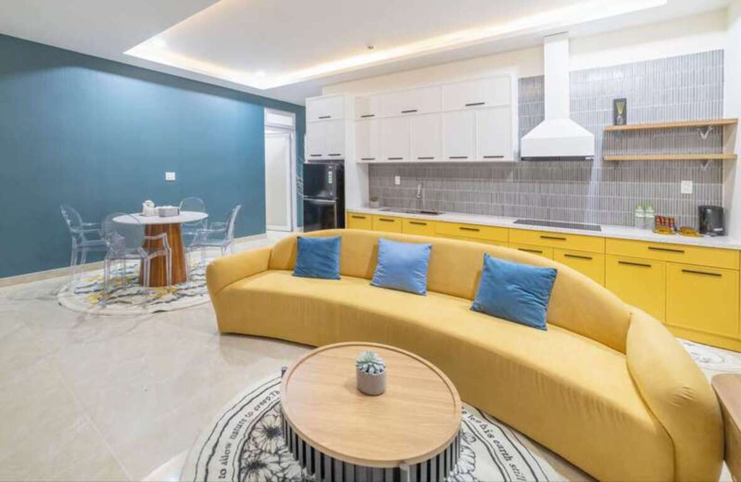 Un salon moderne avec un canapé jaune, une table basse ronde et un coin repas comprenant une petite table et des chaises.