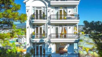 Un edificio de varios pisos con balcones, entrada principal y un área ajardinada.