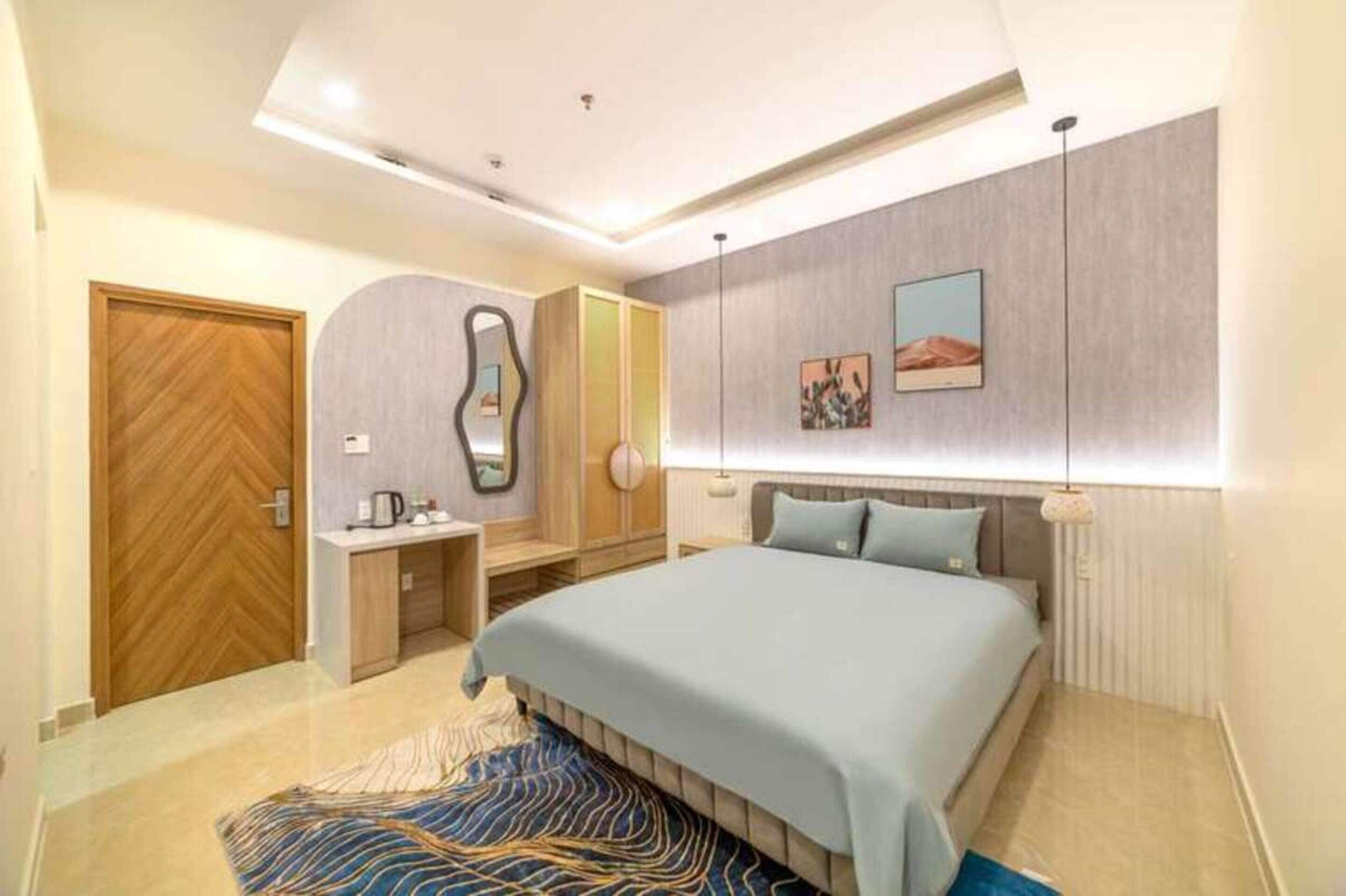 A modern bedroom with a large bed, a desk, and a wardrobe.
