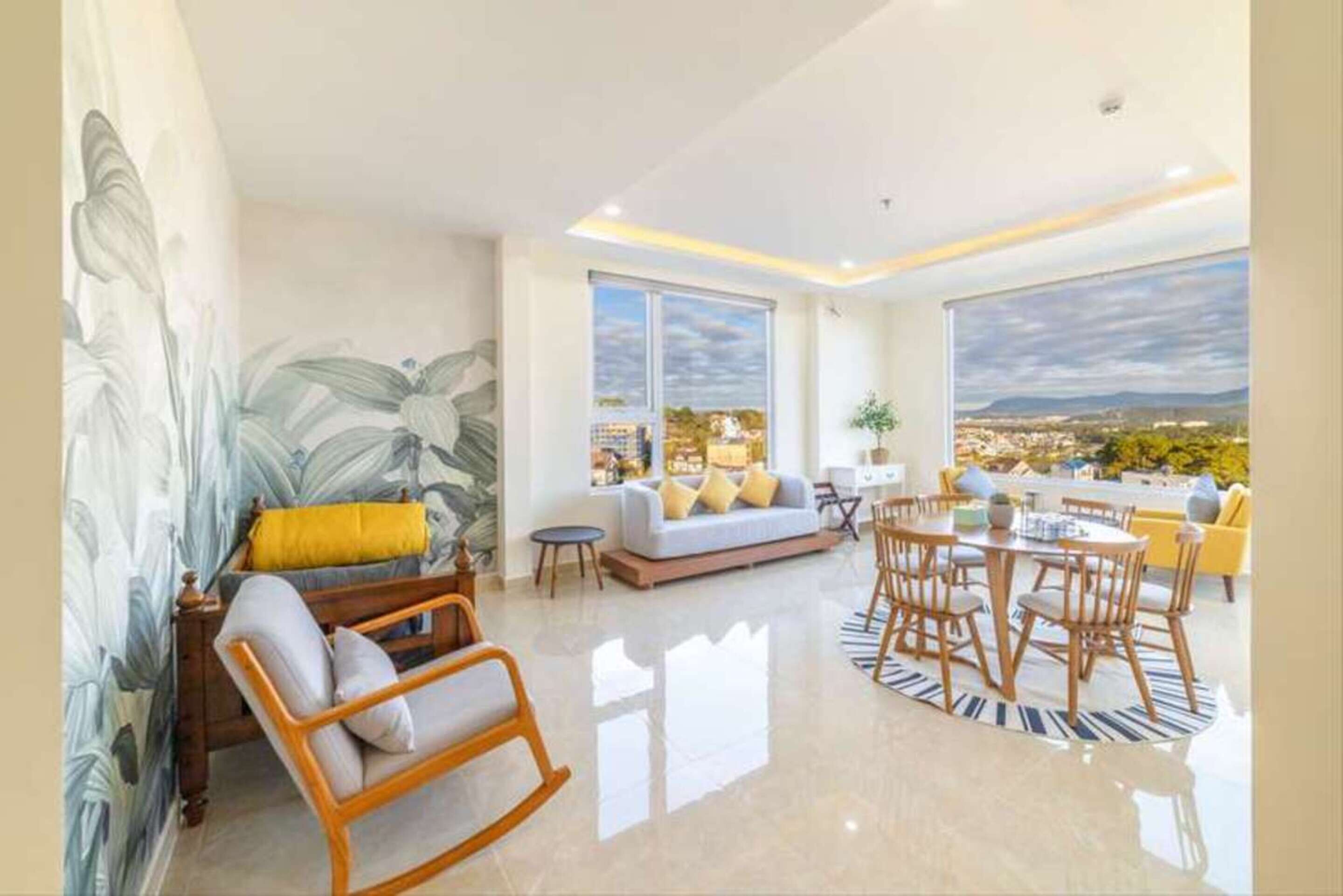 A spacious living area with a large window offering a city view, a cozy seating area with a sofa and chairs, and a dining table with chairs.