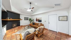 A living room with a fireplace, a ceiling fan, and a door.