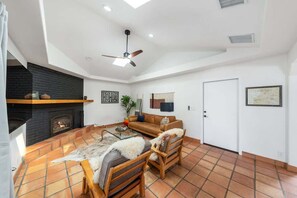 A living room with a fireplace, a ceiling fan, and a door.