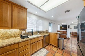 Uma cozinha moderna com armários de madeira, bancadas de granito, lava-louças e piso revestido de azulejos.