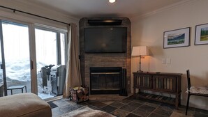 A living room with a fireplace, a television mounted above it, and a large window overlooking a snowy landscape.