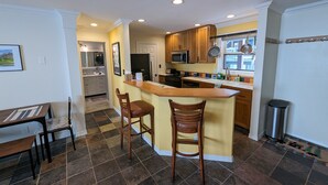 A compact kitchen with a central island, wooden bar stools, and a dining table with chairs.