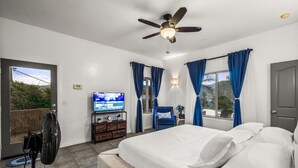 Ein Schlafzimmer mit Bett, Deckenventilator, Fernseher und Blick ins Freie.