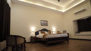 Une chambre à coucher comprenant un lit, des lampes de chevet, une chaise, une fenêtre avec des rideaux et un appareil de climatisation.