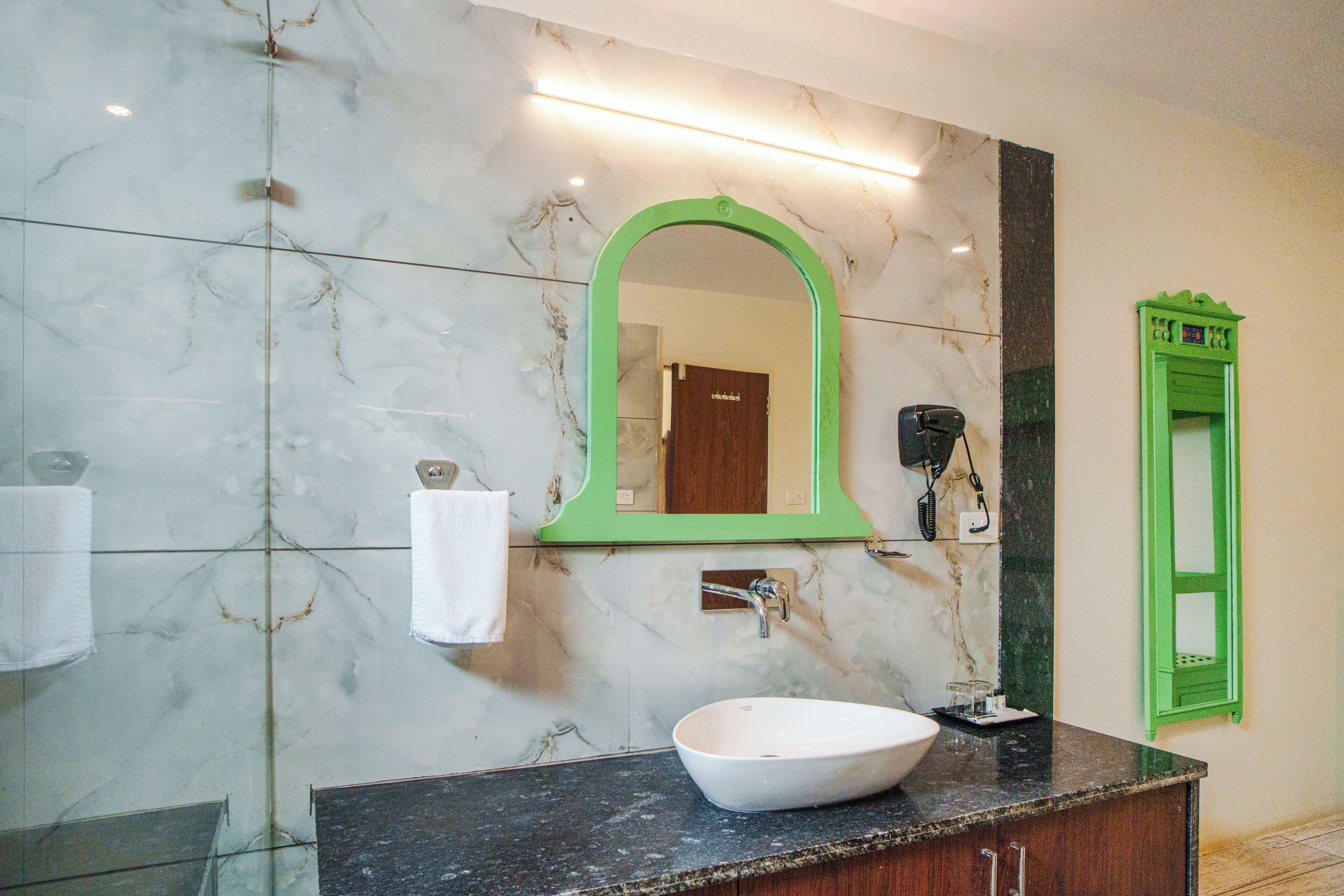 A bathroom with a white sink, a green-framed mirror, and a marble wall.