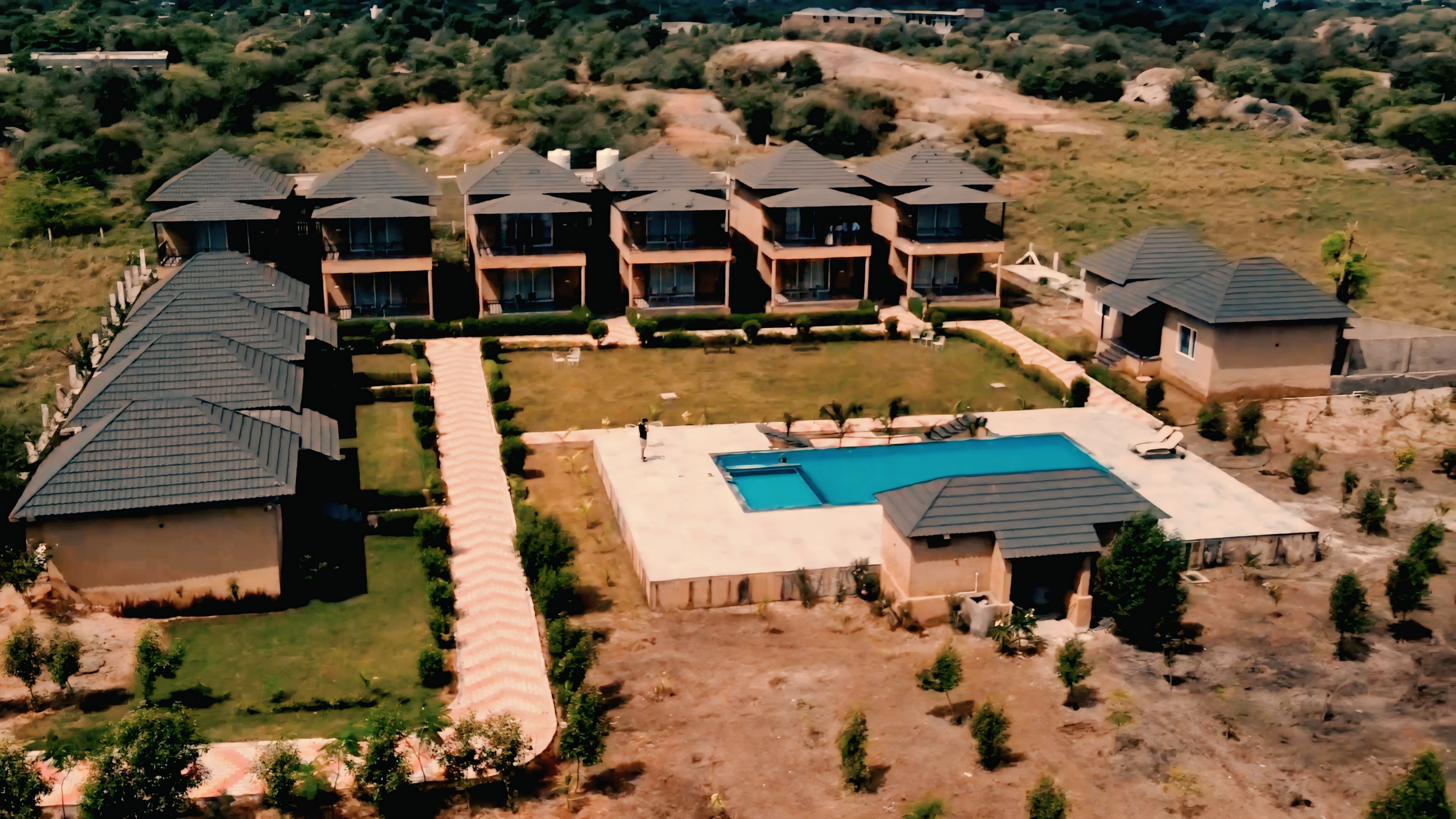 A residential area with multiple houses, a central swimming pool, and a well-maintained lawn.