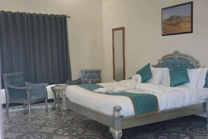 A hotel room with a bed, a chair, a small table, a mirror, and a painting on the wall.