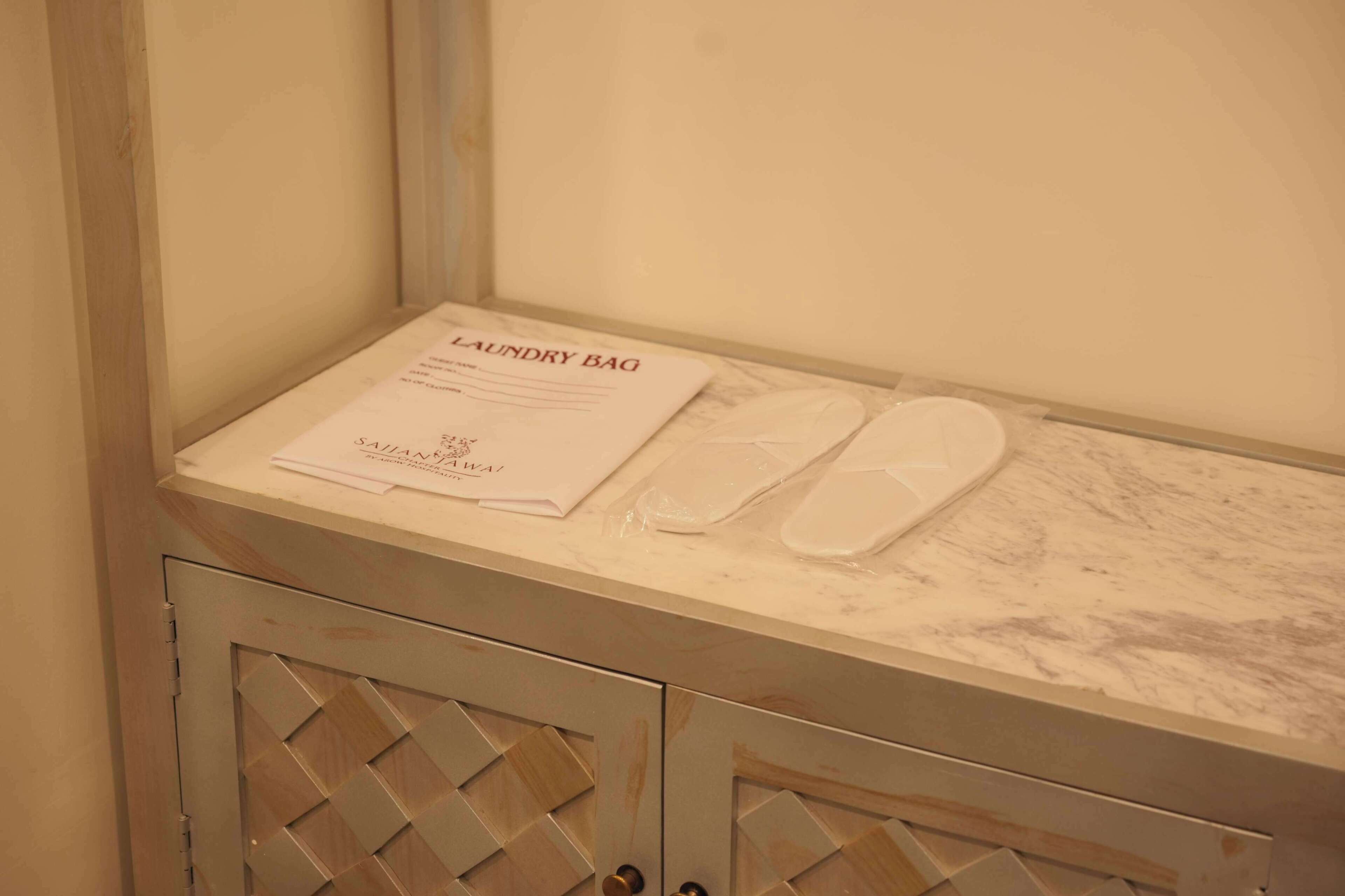A bathroom with a marble countertop, a pair of slippers, and a 'Laundry Bag' sign.