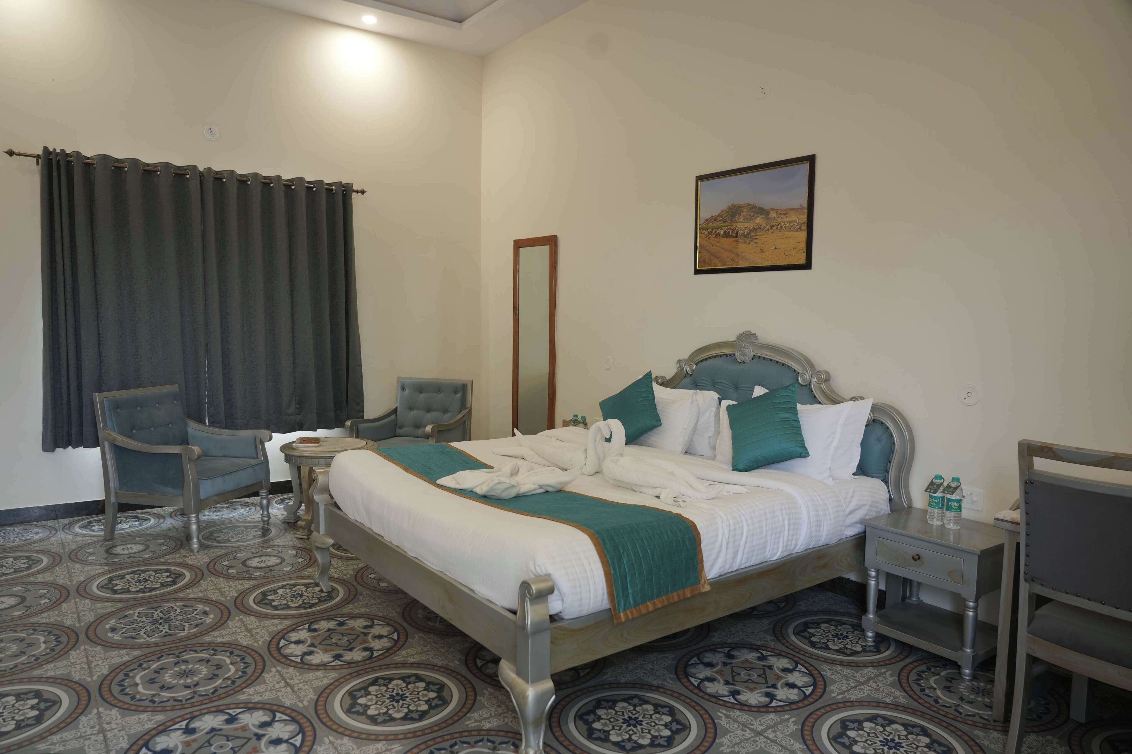 A hotel room with a bed, two chairs, a small table, a nightstand, and a painting on the wall.