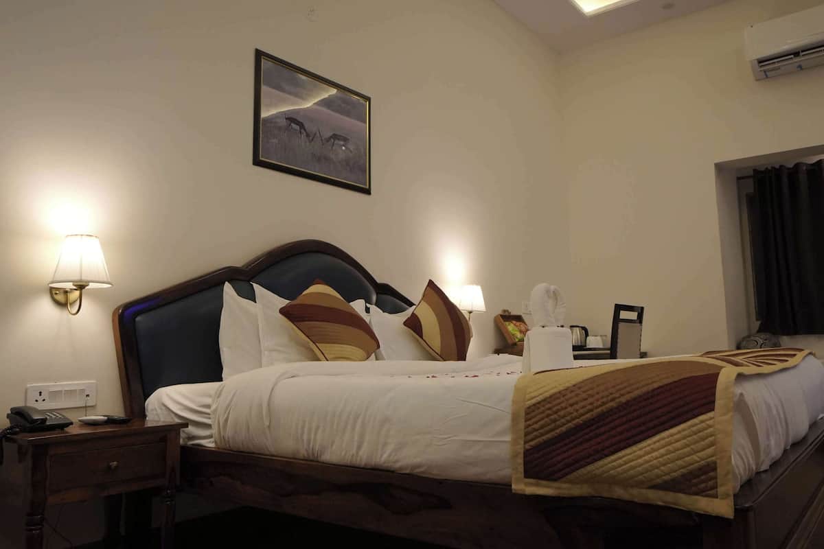 Ein Hotelzimmer mit einem Bett, Nachttischlampen, einem Nachttisch, einem Telefon, einem gerahmten Bild an der Wand und einer Klimaanlage.