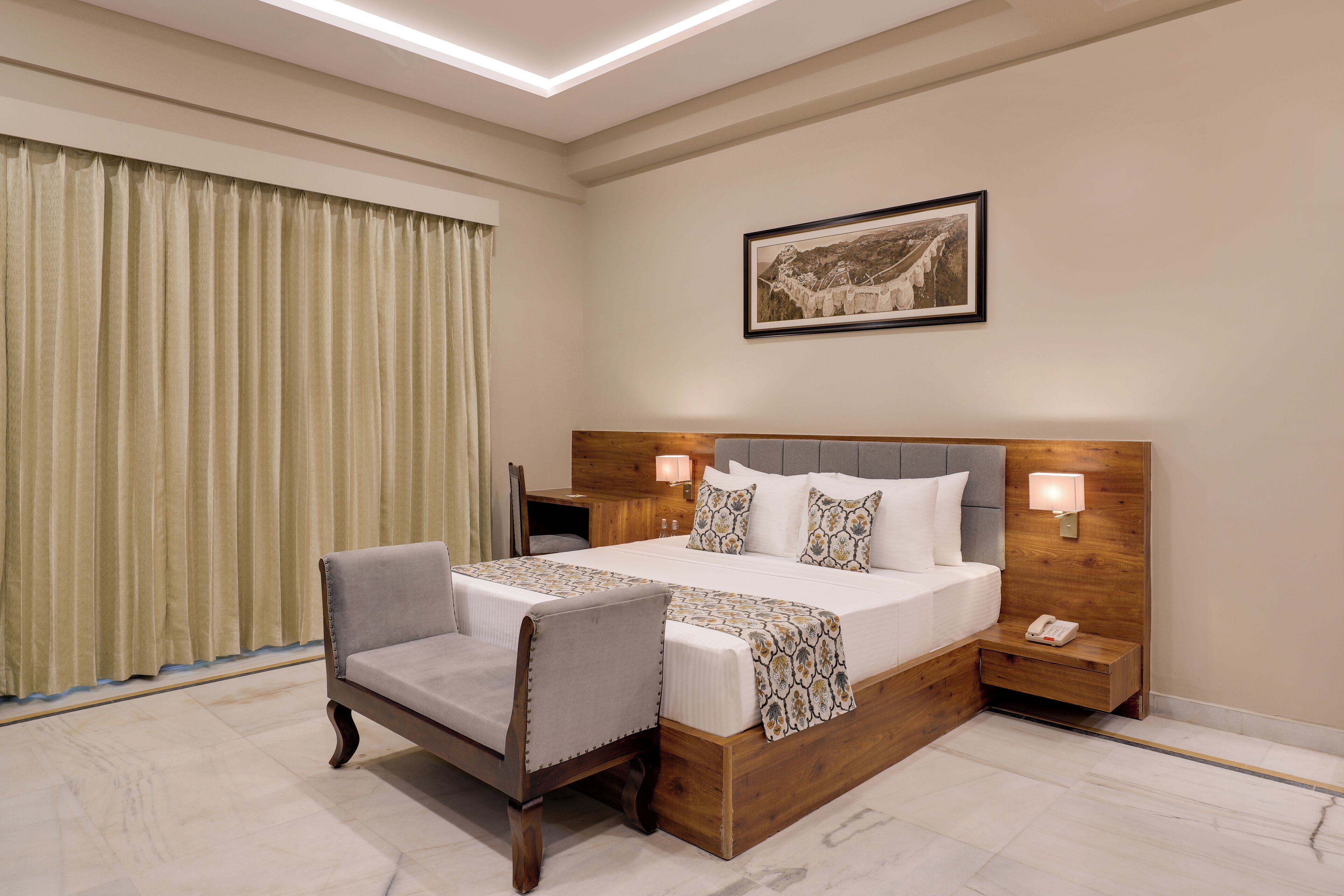 A hotel room with a large bed, a nightstand, a chair, a bedside table, a lamp, and a framed picture on the wall.
