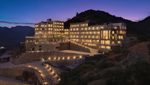 Un hôtel à plusieurs étages doté d’une cour intérieure, entouré de murs et situé au pied d’une chaîne de montagnes.