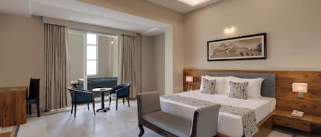 A hotel room with a large bed, a desk, a chair, and a small table.