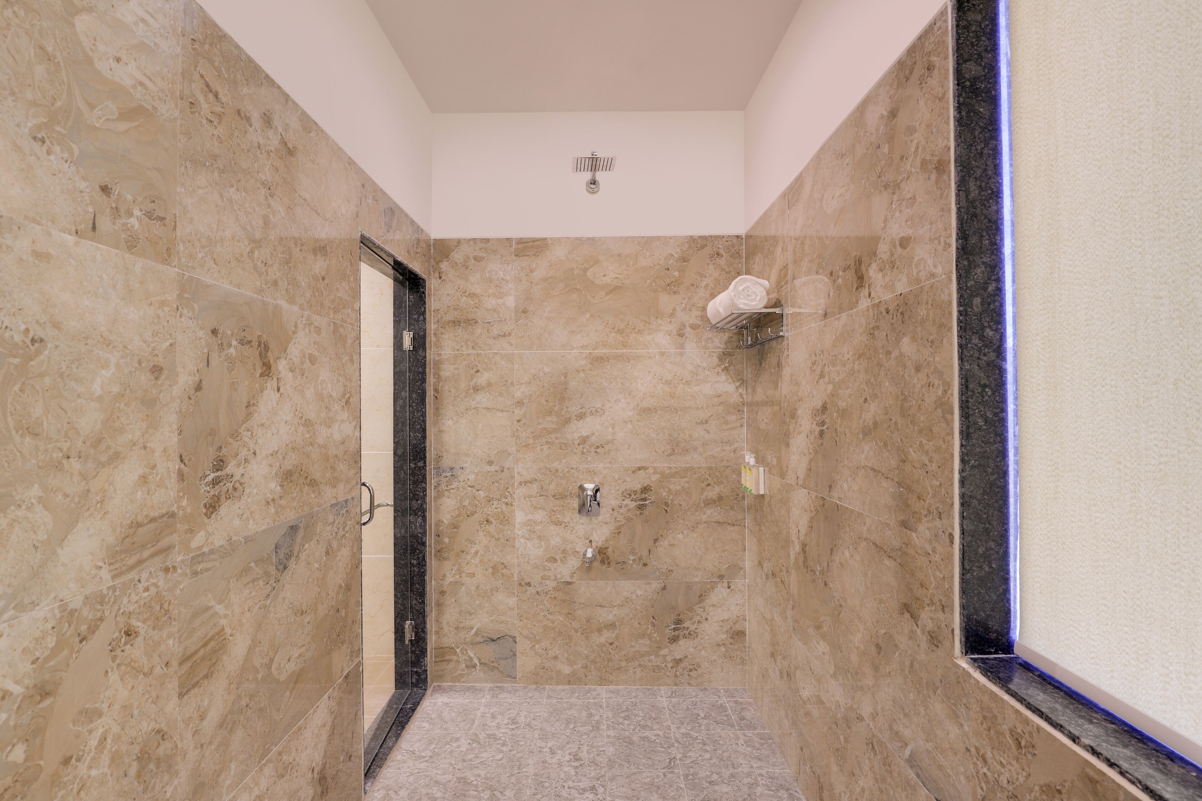 Un baño con paredes de mármol color beige, zona de ducha y un perchero para toallas.