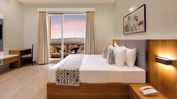 Habitación de hotel con una cama grande, un escritorio, una silla, un balcón con vistas a las montañas y un cuadro en la pared.