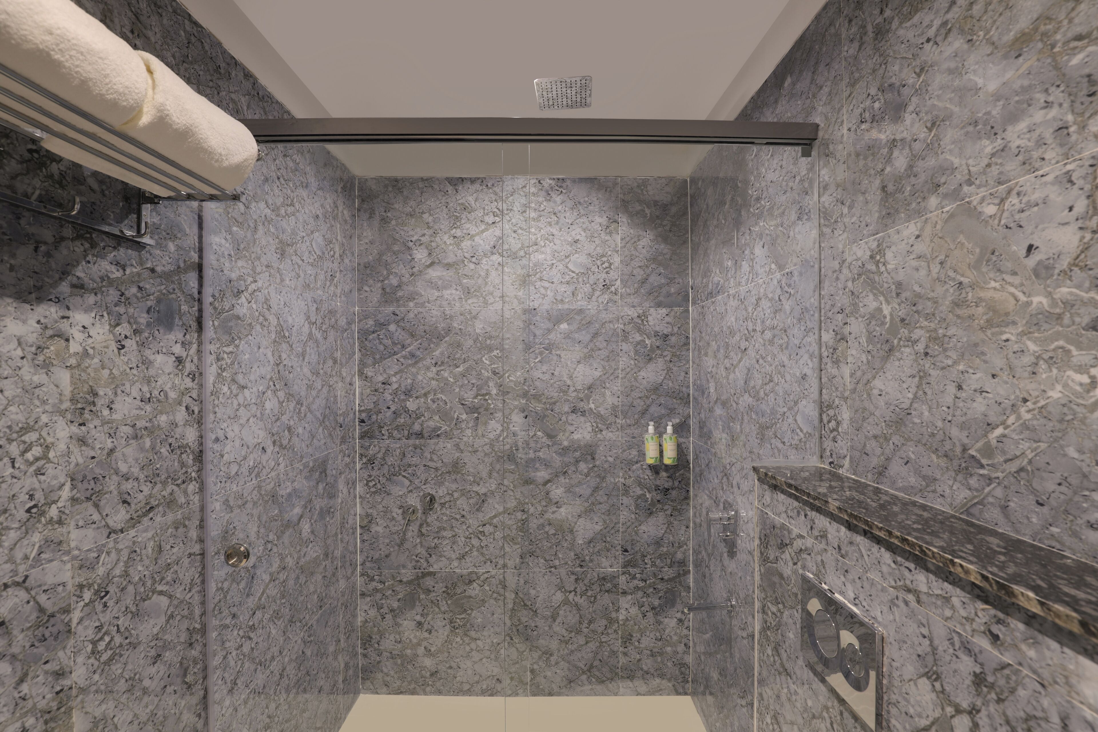 Un baño moderno con ducha envuelta en vidrio, paredes de mármol y un perchero para toallas.