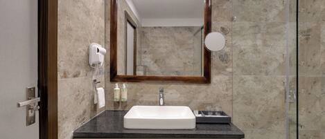 A bathroom with a marble wall, a large mirror, a sink, a hairdryer, and a shower.