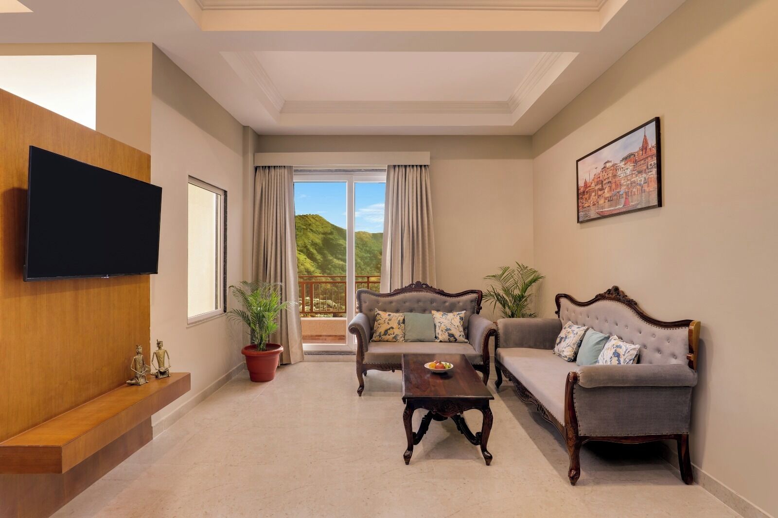 A spacious living room with a large flat-screen TV, two sofas, a coffee table, and a balcony with a scenic view.