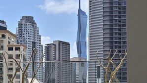 Een modern buitenzitgedeelte met een bank en tafel, omgeven door groen, met uitzicht op een stadsgezicht met hoge gebouwen en een opvallend wolkenkrabber.