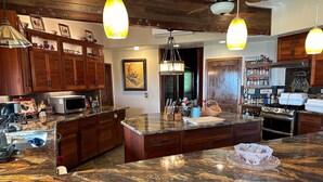A kitchen with granite countertops, wooden cabinets, and pendant lighting. - Magic Skies Main Level Living (Hilo)