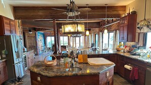 A spacious kitchen with a large island, wooden cabinets, and a stone backsplash. - Magic Skies Main Level Living (Hilo)
