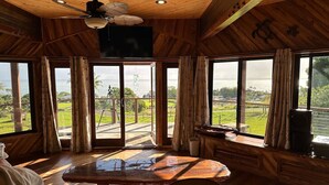 A wooden interior with large windows, a ceiling fan, and a table. - Magic Skies Main Level Living (Hilo)