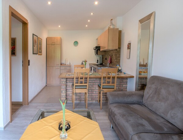 Un salon avec un canapé, un coin repas avec des chaises, une cuisine avec des meubles en bois et une horloge au mur.