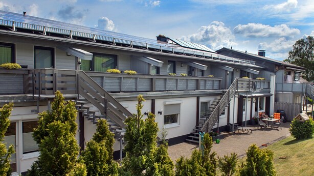 Un bâtiment moderne à plusieurs niveaux, doté d’une terrasse extérieure et d’un patio couvert.