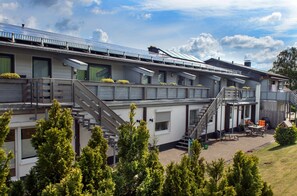 Een modern gebouw met meerdere verdiepingen, terrasplekken en een overdekte patio.