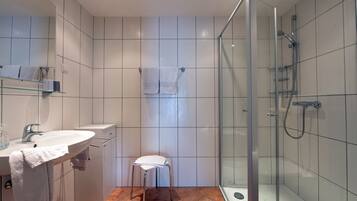 Ein modernes Badezimmer mit einer in Glas abgeschlossenen Dusche, einem Waschbecken mit Handtuch und einem kleinen Hocker.