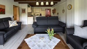 Un salon avec un ensemble de canapés, une table basse ornée d’un vase, et une cuisine en arrière-plan.