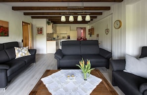 Ein Wohnzimmer mit einer Sofagarnitur, einem Couchtisch mit einer Vase und einer Küche im Hintergrund.